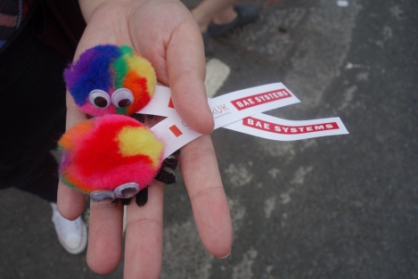 Picture of a hand holding two toys with googly eyes advertising BAE systems that were handed out at the Pride Glasgow march